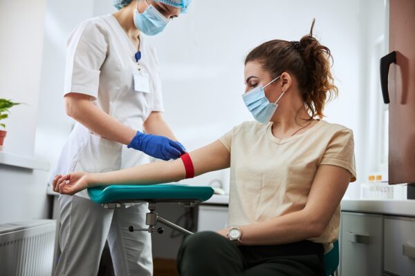 Skilled focused young phlebotomy technician applying a tourniquet to a female patient arm for venipuncture