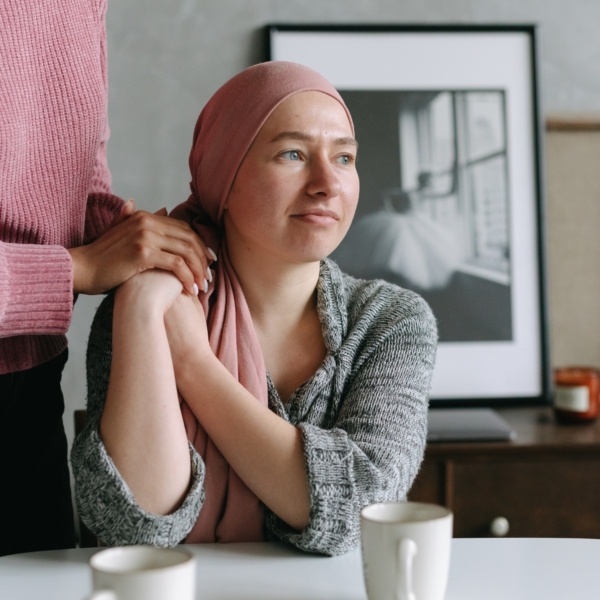 A woman wearing a pink headscarf sat at a table drinking coffee, holding the hand of another person in a pink jumper