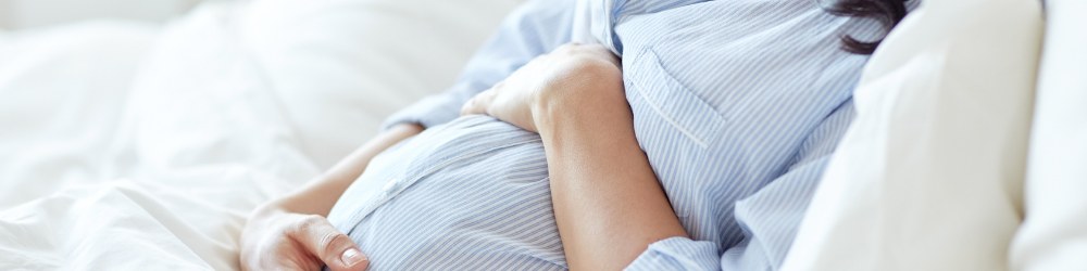 A pregnant woman in a blue shirt lying down holding her stomach