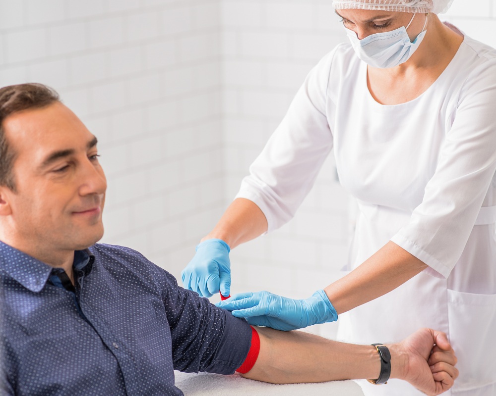 A nurse in white medical wear giving a blood test to a middle aged man